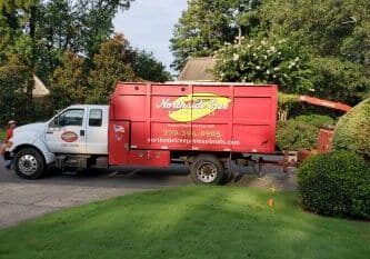 A large red Northwest Tree Service truck is parked on a driveway next to a neatly trimmed lawn and shrubbery, with trees and a house visible in the background.